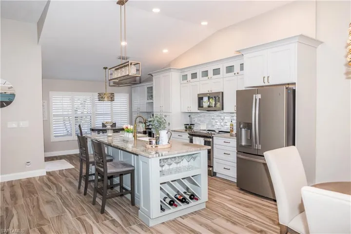 Kitchen featuring hanging light fixtures, appliances with stainless steel finishes, an island with sink, light stone countertops, and white cabinets