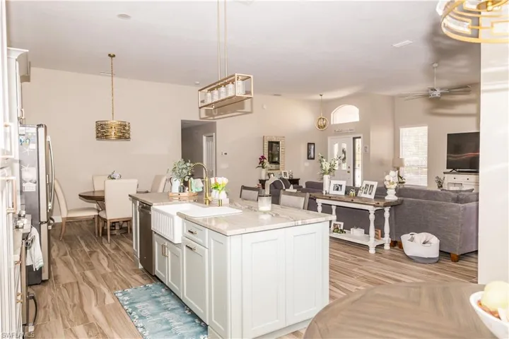Kitchen with appliances with stainless steel finishes, white cabinetry, hanging light fixtures, light stone counters, and a center island with sink