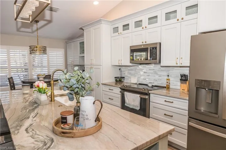 Kitchen featuring light stone counters, tasteful backsplash, decorative light fixtures, stainless steel appliances, and white cabinets