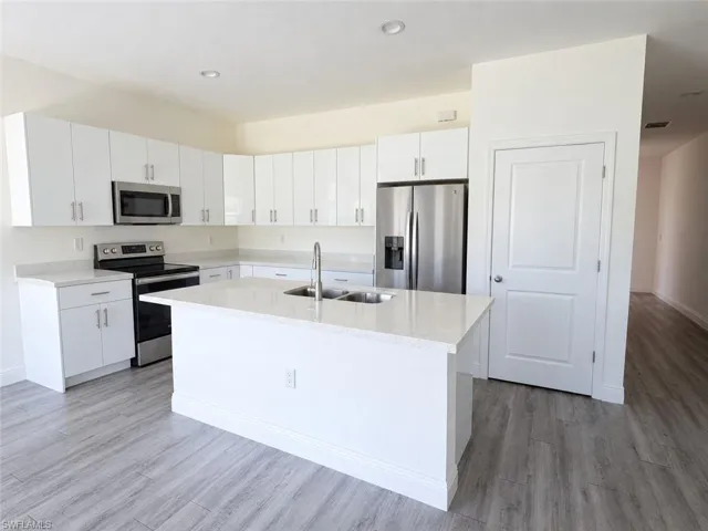 Modern kitchen featuring an island, stainless steel appliances, white cabinetry, and light-toned countertops