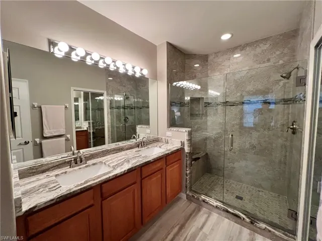Beautifully renovated Bathroom with granite counters, wood cabinets, dual sinks, tile shower, glass shower door and tile floor.