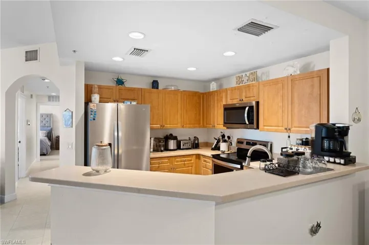 Kitchen with appliances with stainless steel finishes, arched walkways, light countertops, a peninsula, and light tile patterned floors