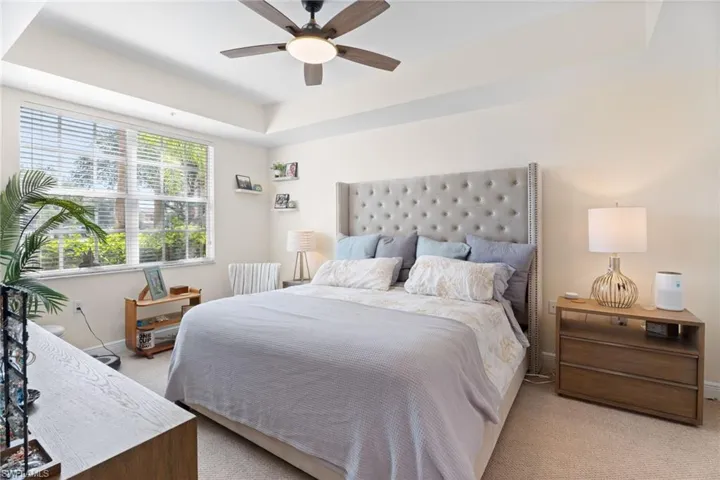 Bedroom with light carpet, ceiling fan, and a raised ceiling