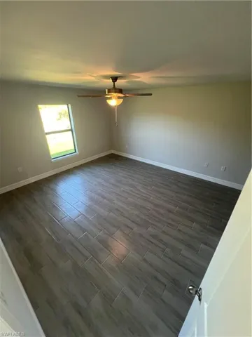 Unfurnished room with dark wood-style floors, baseboards, and ceiling fan