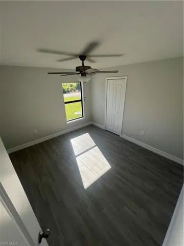 Unfurnished room featuring baseboards, dark wood-style flooring, and ceiling fan