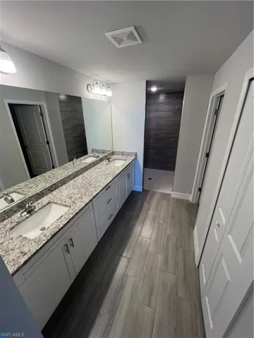 Bathroom featuring visible vents, wood finish floors, walk in shower, double vanity, and a sink