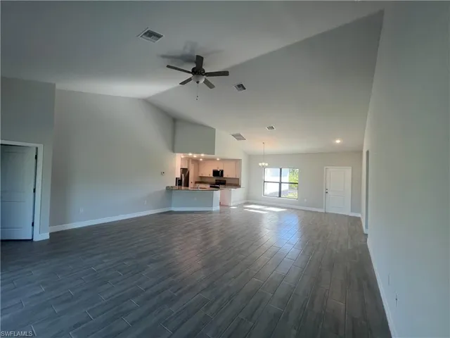 Unfurnished living room featuring vaulted ceiling, dark wood-style floors, ceiling fan with notable chandelier, and visible vents
