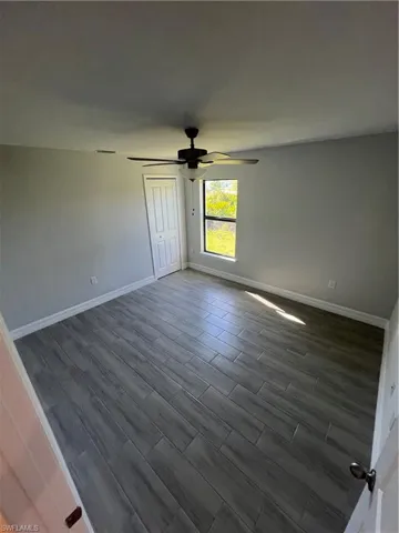 Unfurnished room with dark wood-style floors, baseboards, and ceiling fan