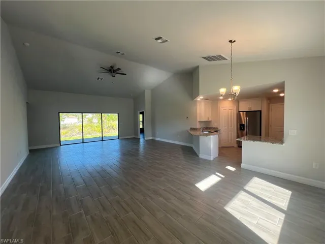 Unfurnished living room featuring ceiling fan with notable chandelier, baseboards, visible vents, and dark wood-style flooring