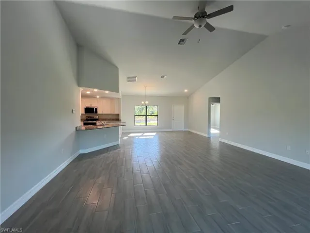 Unfurnished living room with dark wood-type flooring, ceiling fan with notable chandelier, visible vents, and baseboards
