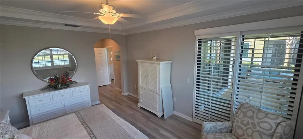 Bedroom with arched walkways, a ceiling fan, wood finished floors, crown molding, and a raised ceiling