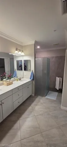 Bathroom featuring double vanity, crown molding, a shower stall, and radiator heating unit