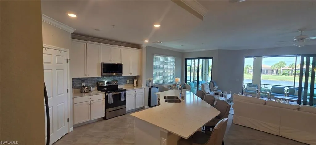 Kitchen featuring open floor plan, stainless steel appliances, white cabinets, a kitchen breakfast bar, and an island with sink