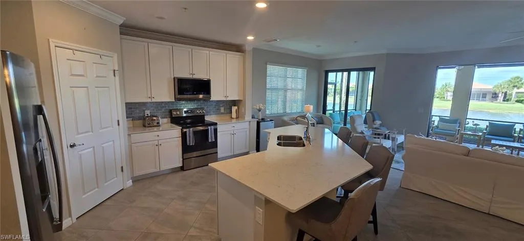 Kitchen with a breakfast bar area, white cabinetry, stainless steel appliances, open floor plan, and ornamental molding