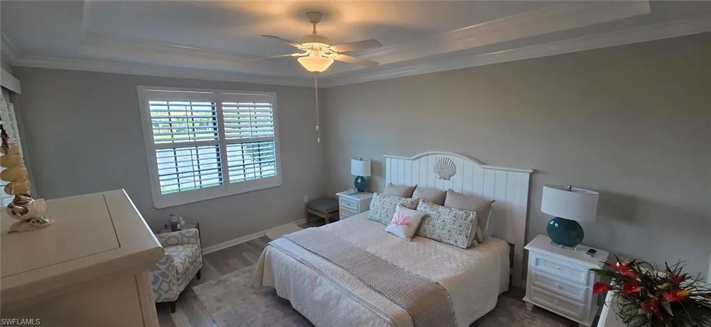 Bedroom with a raised ceiling, ceiling fan, wood finished floors, and crown molding