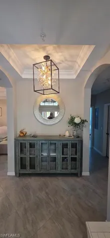 Bar featuring arched walkways, ornamental molding, a tray ceiling, and hanging lights