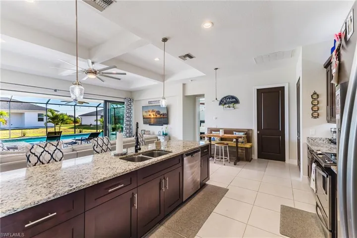 Kitchen with open floor plan, light stone countertops, dark brown cabinetry, stainless steel appliances, and recessed lighting