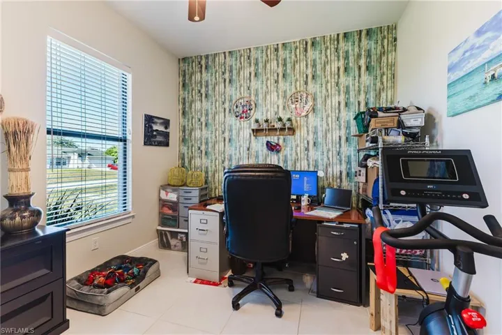 Office space with an accent wall, a ceiling fan, light tile patterned flooring, and wallpapered walls