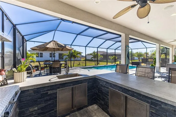 View of patio featuring a sunroom, an outdoor kitchen, outdoor dining space, glass enclosure, and a ceiling fan