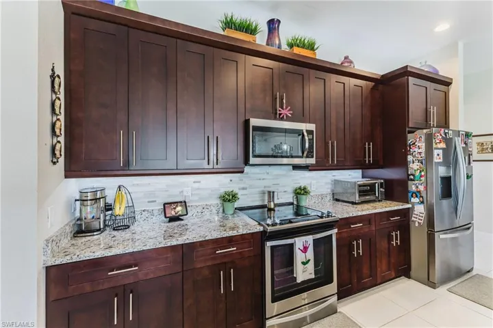 Kitchen with stainless steel appliances, light stone counters, backsplash, and light tile patterned floors