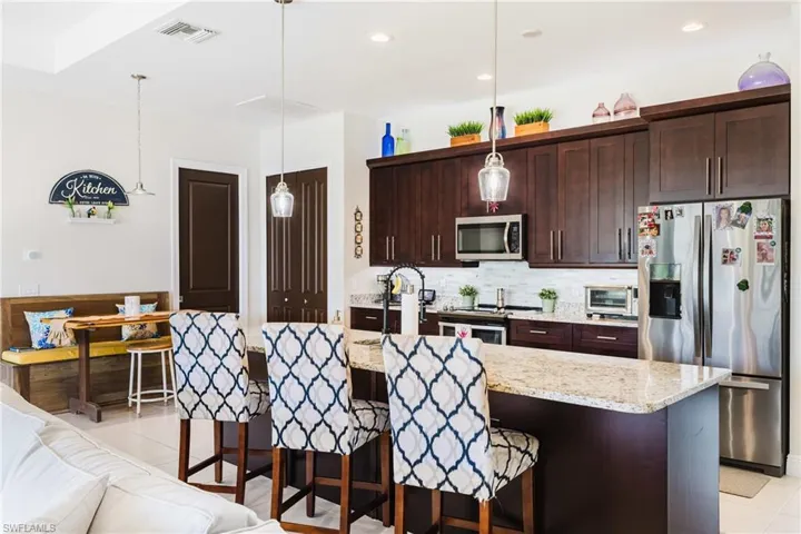 Kitchen with a breakfast bar area, pendant lighting, stainless steel appliances, dark brown cabinetry, and light stone countertops
