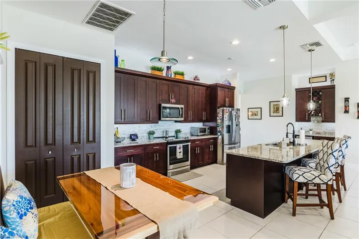 Kitchen featuring a breakfast bar area, dark brown cabinetry, light stone countertops, appliances with stainless steel finishes, and decorative light fixtures
