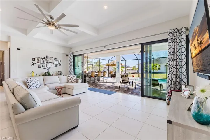 Living area with a sunroom, ceiling fan, coffered ceiling, light tile patterned floors, and recessed lighting