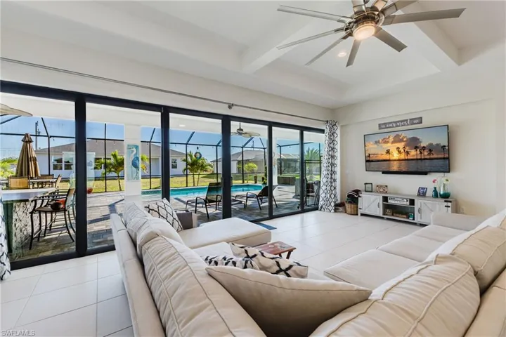 Living area with a sunroom, light tile patterned flooring, ceiling fan, beam ceiling, and coffered ceiling