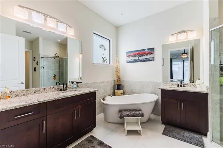 Bathroom featuring two vanities, tile walls, a shower stall, a freestanding bath, and wainscoting