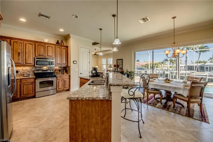 Kitchen featuring suspended lighting, stainless steel appliances, a kitchen bar, ornamental molding, and wood finish cabinetry