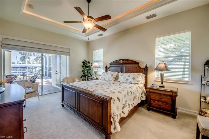 Bedroom featuring light colored carpet, a raised ceiling, access to exterior, and a ceiling fan
