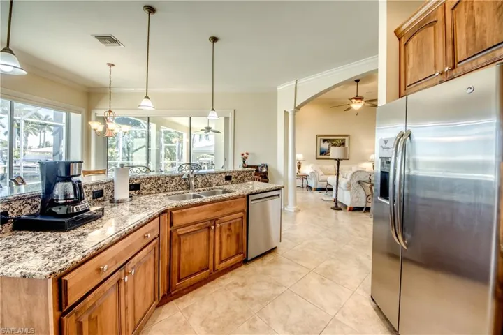 Kitchen featuring wood finish cabinets, stainless steel appliances, ceiling fan, light stone countertops, and ornamental molding