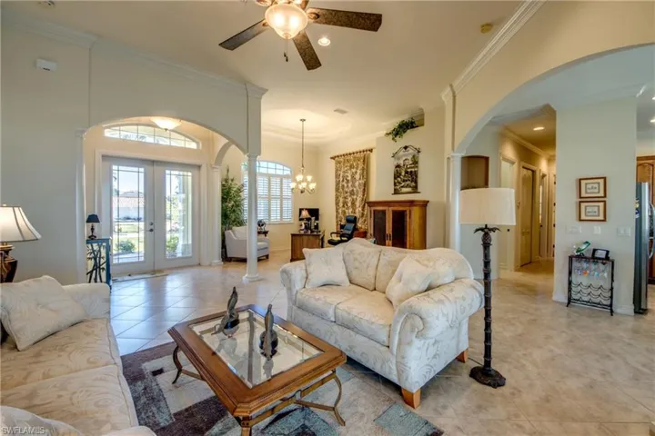 Living area with arched walkways, a ceiling fan, crown molding, french doors, and light tile patterned floors