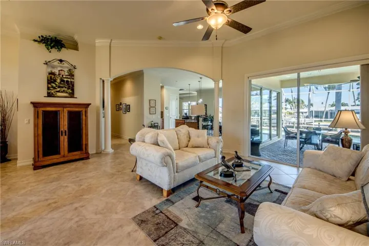 Living area featuring crown molding, ceiling fan, arched walkways, decorative columns, and light tile patterned floors