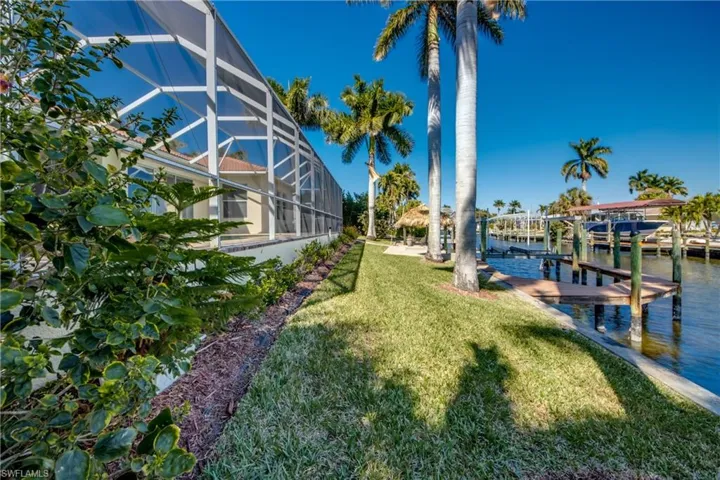 Dock featuring a sunroom, a lawn, boat lift, a water view, and glass enclosure
