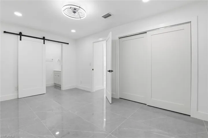 Unfurnished bedroom featuring a barn door, connected bathroom, recessed lighting, and a closet