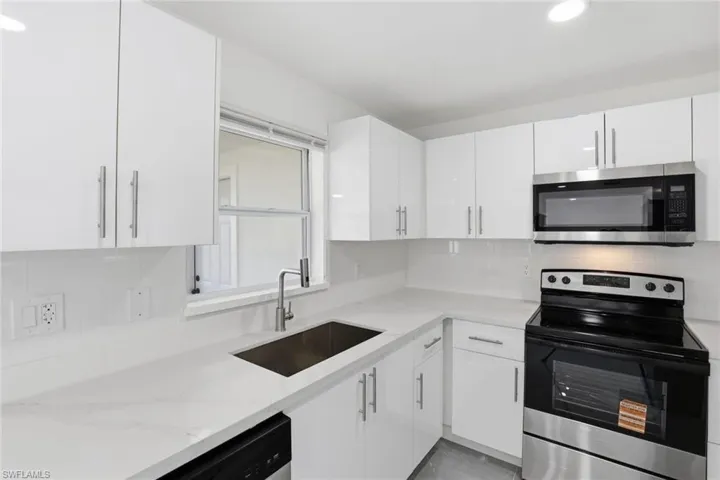 Kitchen featuring stainless steel appliances, backsplash, white cabinetry, light stone counters, and recessed lighting