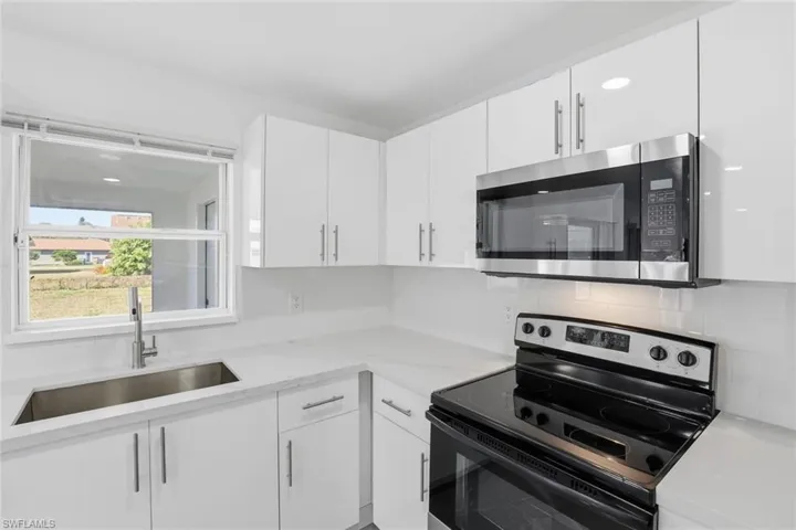 Kitchen with electric stove, stainless steel microwave, white cabinetry, and light stone counters