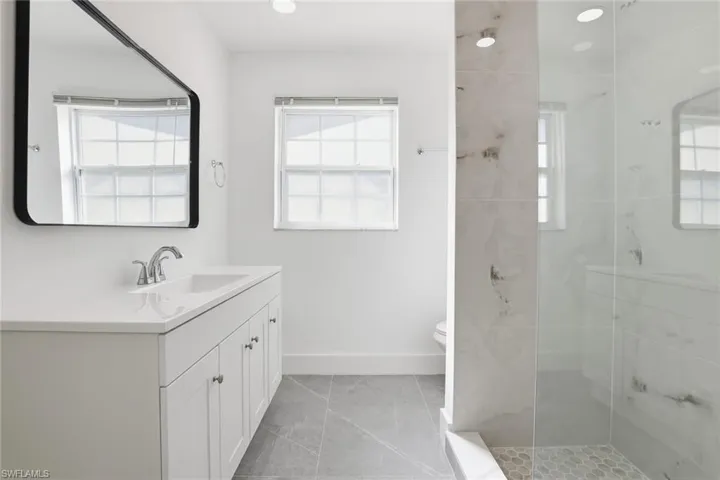 Full bath with vanity, tiled shower, light tile patterned floors, and recessed lighting