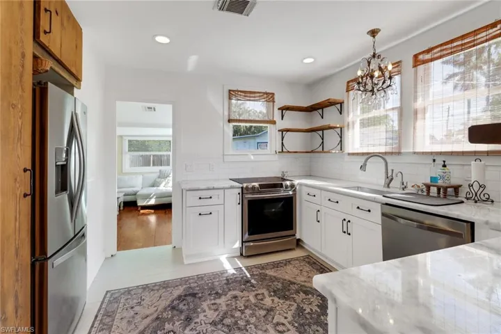 Kitchen with stainless steel appliances, light stone countertops, and white cabinets