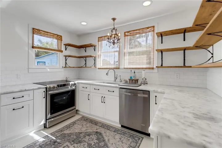 Kitchen with sink, appliances with stainless steel finishes, hanging light fixtures, light stone countertops, and white cabinets