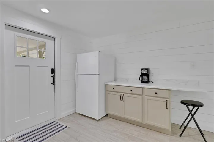 Kitchen featuring freestanding refrigerator, light stone counters, wooden walls, light wood-style flooring, and cream cabinetry