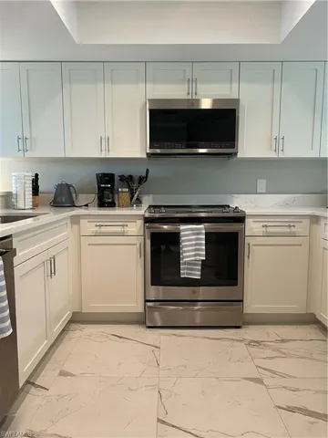 Kitchen featuring a raised ceiling, stainless steel range oven, light tile patterned floors, and white cabinetry