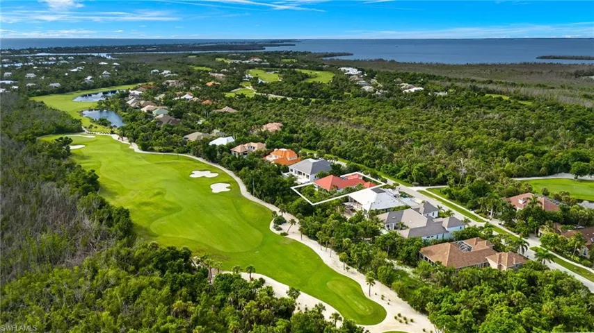 Aerial view of residential area with a nearby body of water, property boundaries highlighted, and a golf club