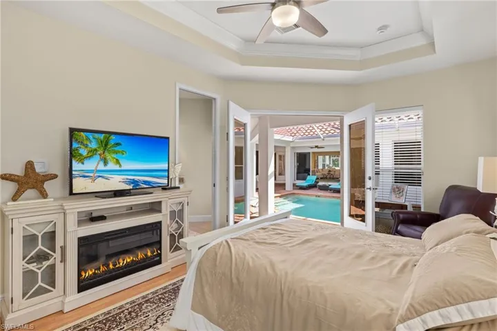 Bedroom with a tray ceiling, a glass covered fireplace, ornamental molding, light wood-style flooring, and ceiling fan