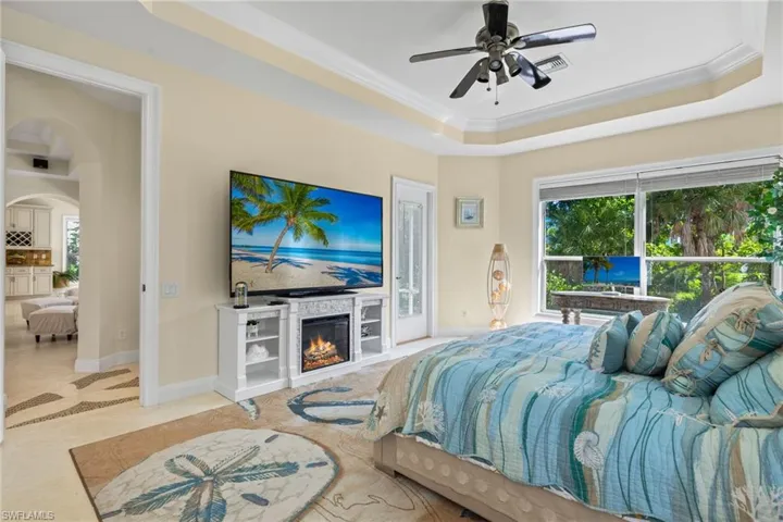 Tiled bedroom featuring a tray ceiling, ornamental molding, arched walkways, and a ceiling fan