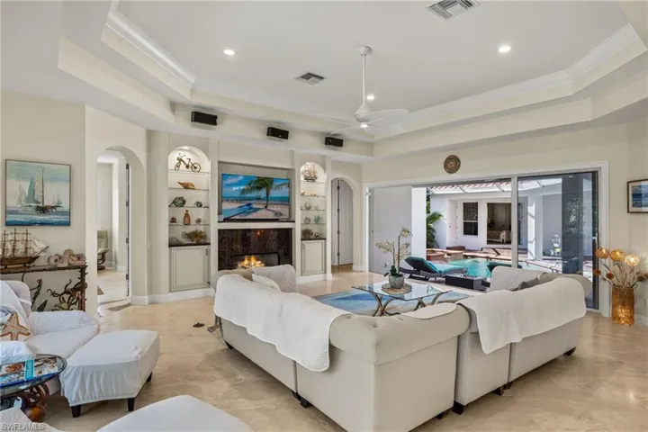 Living room featuring built in features, ceiling fan, ornamental molding, a raised ceiling, and a high end fireplace