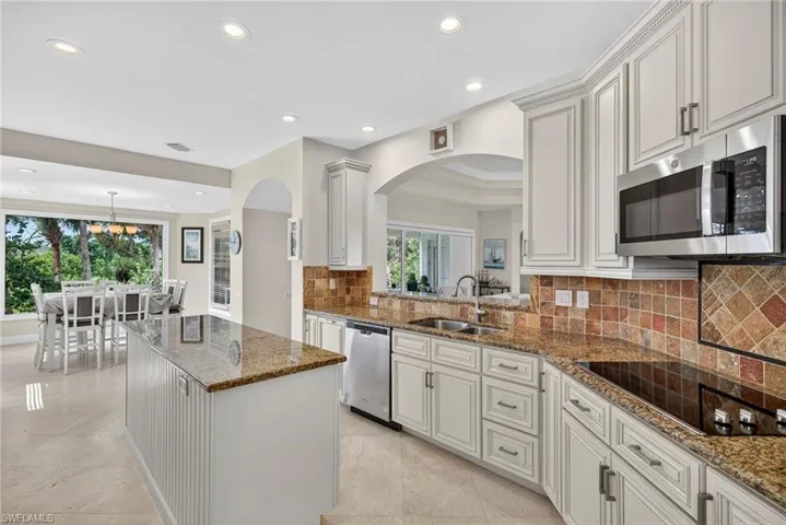 Kitchen with dark stone countertops, backsplash, stainless steel appliances, arched walkways, and recessed lighting