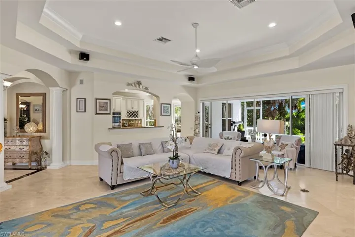 Living room featuring arched walkways, ornamental molding, a tray ceiling, ceiling fan, and decorative columns