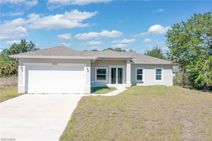 View of front of house with french doors, a front lawn, stucco siding, a garage, and driveway